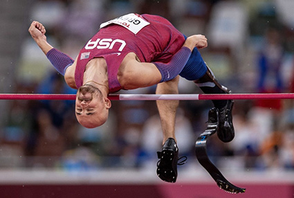 Athlete doing backflip over Olympic high bar with leg prosthetic