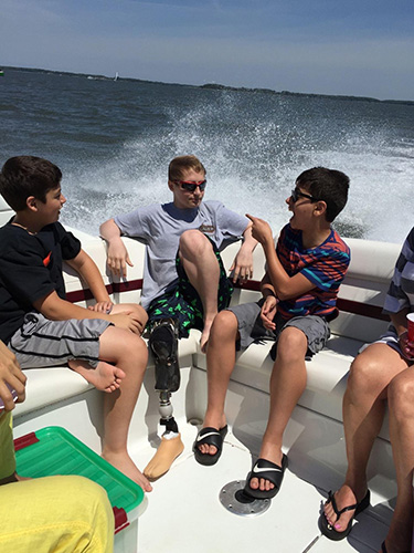 Male with leg prosthetic sits with group of friends on a boat