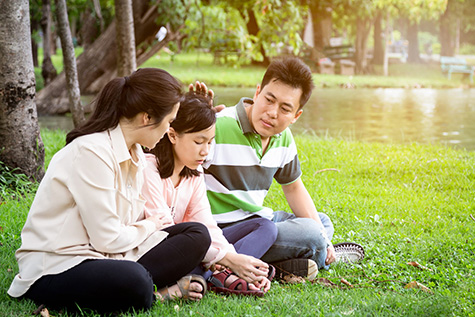 Family of three sits by pond
