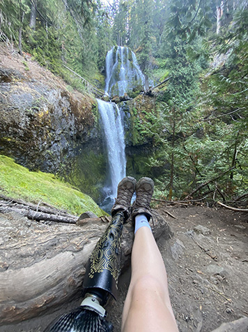 Hiker with leg prosthetic sits and looks at waterfall