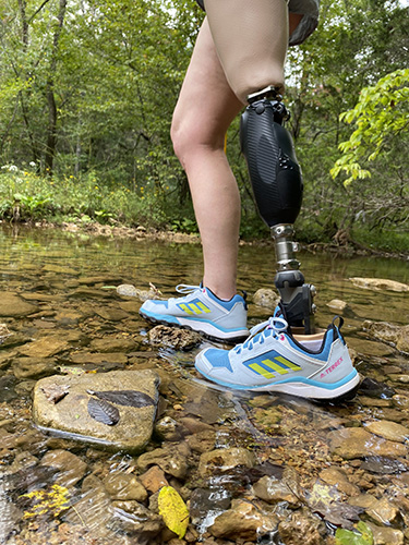 Individual hiking through creek with amputation and leg prosthetic