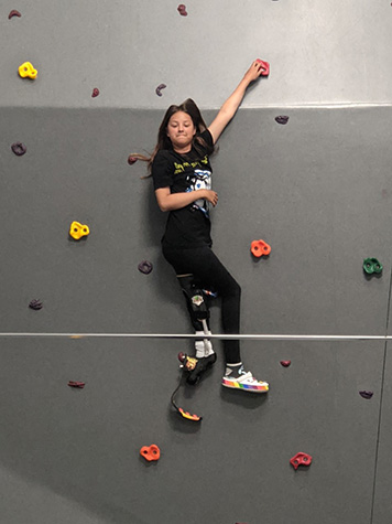 Female on rock climbing wall with blade leg prosthetic